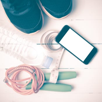 fitness equipment : running shoes,jumping rope,drinking water,measuring tape and phone on white wood table vintage style