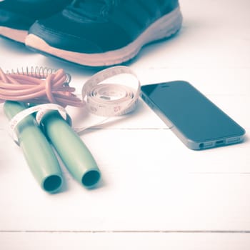 fitness equipment : running shoes,jumping rope,measuring tape and phone on white wood table vintage style