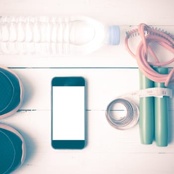 fitness equipment : running shoes,jumping rope,drinking water,measuring tape and phone on white wood table vintage style