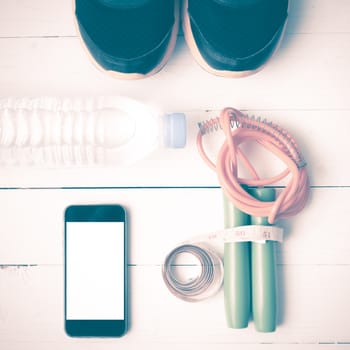 fitness equipment : running shoes,jumping rope,drinking water,measuring tape and phone on white wood table vintage style