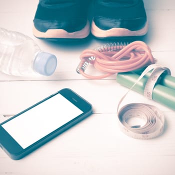 fitness equipment : running shoes,jumping rope,drinking water,measuring tape and phone on white wood table vintage style