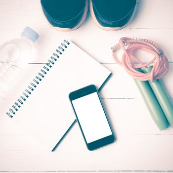 fitness equipment : running shoes,jumping rope,drinking water,notebook and phone on white wood table vintage style