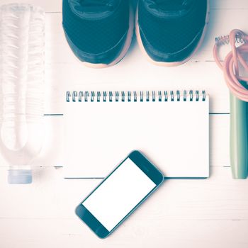 fitness equipment : running shoes,jumping rope,drinking water,notebook and phone on white wood table vintage style