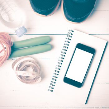 fitness equipment : running shoes,jumping rope,drinking water,notebook,measuring tape and phone on white wood table vintage style