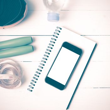 fitness equipment : running shoes,jumping rope,drinking water,notebook,measuring tape and phone on white wood table vintage style