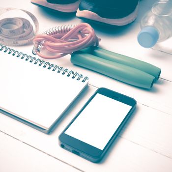 fitness equipment : running shoes,jumping rope,drinking water,notebook,measuring tape and phone on white wood table vintage style