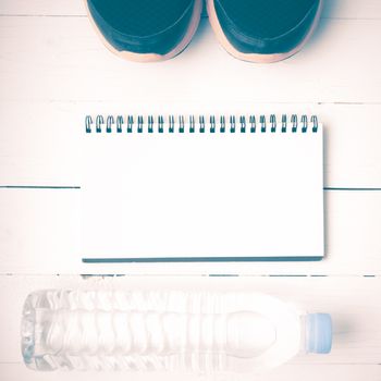 fitness equipment : running shoes,drinking water and notebook on white wood table vintage style