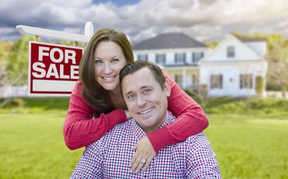 Happy Couple In Front of For Sale Real Estate Sign and Beautiful House.