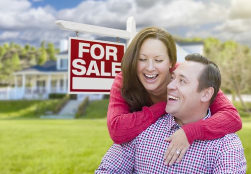 Happy Laughing Couple In Front of For Sale Real Estate Sign and Beautiful House.