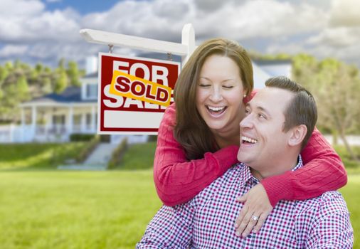 Happy Laughing Couple In Front of Sold For Sale Real Estate Sign and Beautiful House.