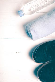 fitness equipment:blue towel,drinking water and running shoes on white wood table vintage style