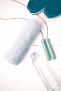 fitness equipment : running shoes,towel,jumping rope and drinking water on white wood table vintage style