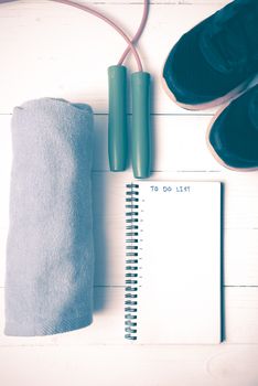 fitness equipment : running shoes,towel,jumping rope and notebook write to do list on white wood table vintage style