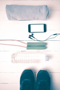 fitness equipment : running shoes,towel,jumping rope,water bottle and phone on white wood table vintage style