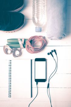 fitness equipment : running shoes,towel,jumping rope,water bottle,phone,notepad and measuring tape on white wood table vintage style