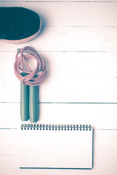 fitness equipment : running shoes,jumping rope and notepad on white wood table vintage style