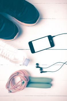 fitness equipment : running shoes,jumping rope,phone and water bottle on white wood table vintage style