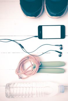 fitness equipment : running shoes,jumping rope,phone and water bottle on white wood table vintage style