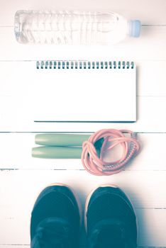 fitness equipment : running shoes,jumping rope,drinking water and notepad on white wood table vintage style