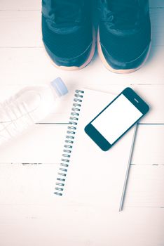 fitness equipment : running shoes,drinking water,notebook and phone on white wood table vintage style