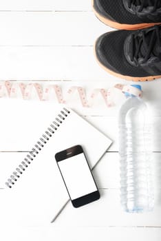running shoes,measuring tape,drinking water,notebook and phone on white wood table