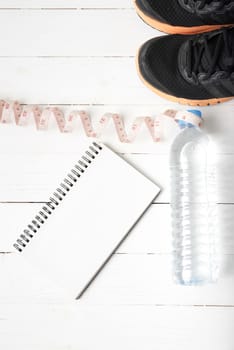 running shoes,measuring tape,drinking water and notebook on white wood table