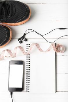 running shoes,measuring tape,notebook and phone on white wood table