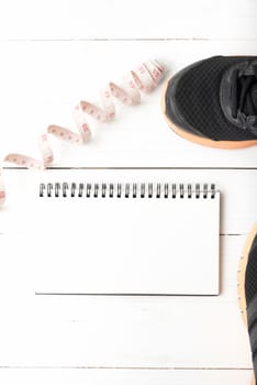 running shoes with notebook and measuring tape on white wood table