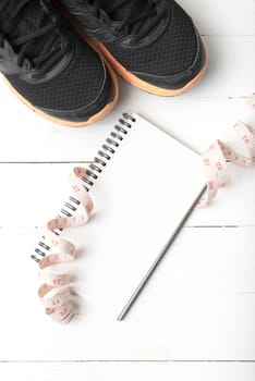 running shoes with notebook and measuring tape on white wood table