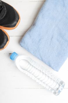 fitness equipment:blue towel,drinking water and running shoes on white wood table