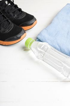 fitness equipment:blue towel,drinking water and running shoes on white wood table