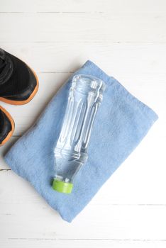 fitness equipment:blue towel,drinking water and running shoes on white wood table