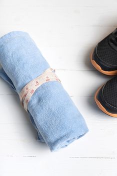 fitness equipment : running shoes,blue towel and measuring tape on white wood table