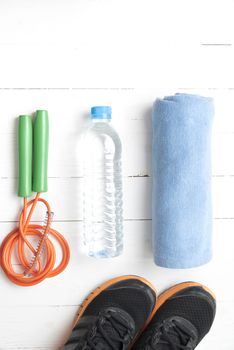 fitness equipment : running shoes,towel,jumping rope and drinking water on white wood table