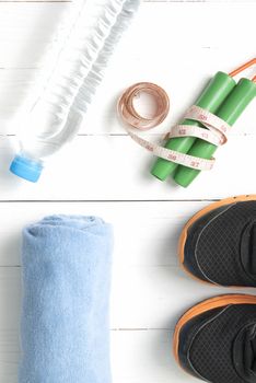 fitness equipment : running shoes,towel,jumping rope,water bottle and measuring tape on white wood table
