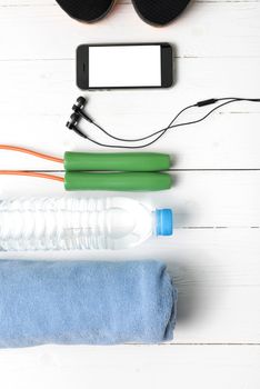 fitness equipment : running shoes,towel,jumping rope,water bottle and phone on white wood table