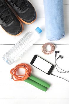 fitness equipment : running shoes,towel,jumping rope,water bottle,phone and measuring tape on white wood table