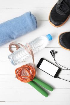 fitness equipment : running shoes,towel,jumping rope,water bottle,phone and measuring tape on white wood table