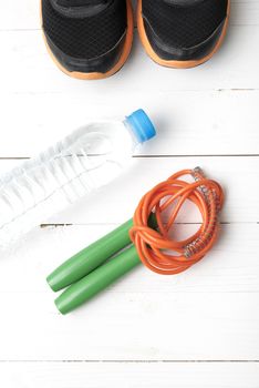 fitness equipment : running shoes,jumping rope and water bottle on white wood table