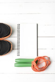 fitness equipment : running shoes,jumping rope and notepad on white wood table