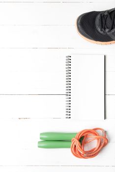 fitness equipment : running shoes,jumping rope and notepad on white wood table