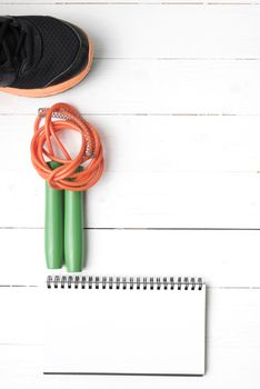 fitness equipment : running shoes,jumping rope and notepad on white wood table