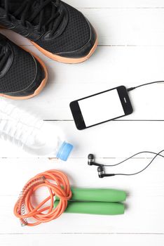 fitness equipment : running shoes,jumping rope,phone and water bottle on white wood table