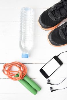 fitness equipment : running shoes,jumping rope,phone and water bottle on white wood table