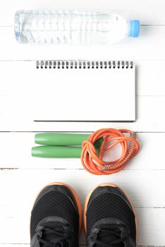 fitness equipment : running shoes,jumping rope,drinking water and notepad on white wood table