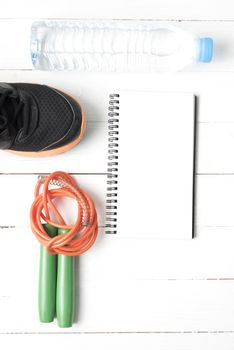 fitness equipment : running shoes,jumping rope,drinking water and notepad on white wood table