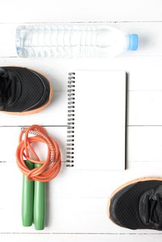 fitness equipment : running shoes,jumping rope,drinking water and notepad on white wood table