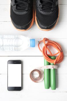 fitness equipment : running shoes,jumping rope,drinking water,measuring tape and phone on white wood table