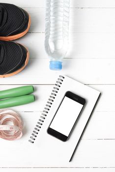 fitness equipment : running shoes,jumping rope,drinking water,notebook,measuring tape and phone on white wood table