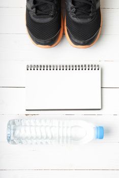 fitness equipment : running shoes,drinking water and notebook on white wood table